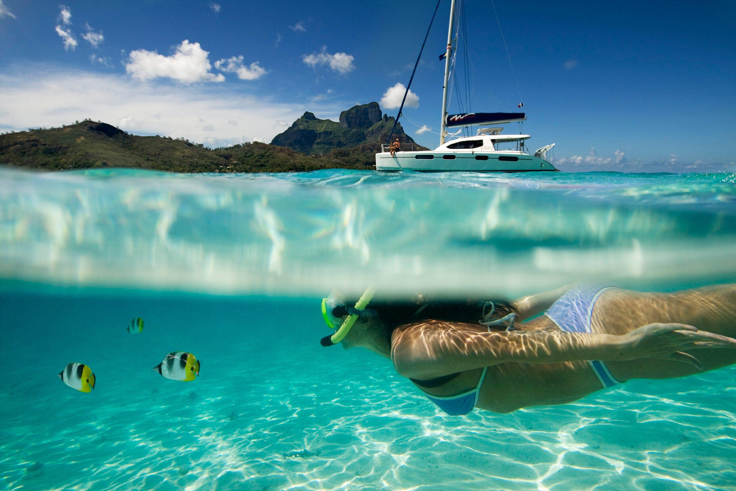 A high-angle shot of catamarans anchored in a crystal-clear turquoise lagoon surrounded by lush green tropical islands in Tahiti.